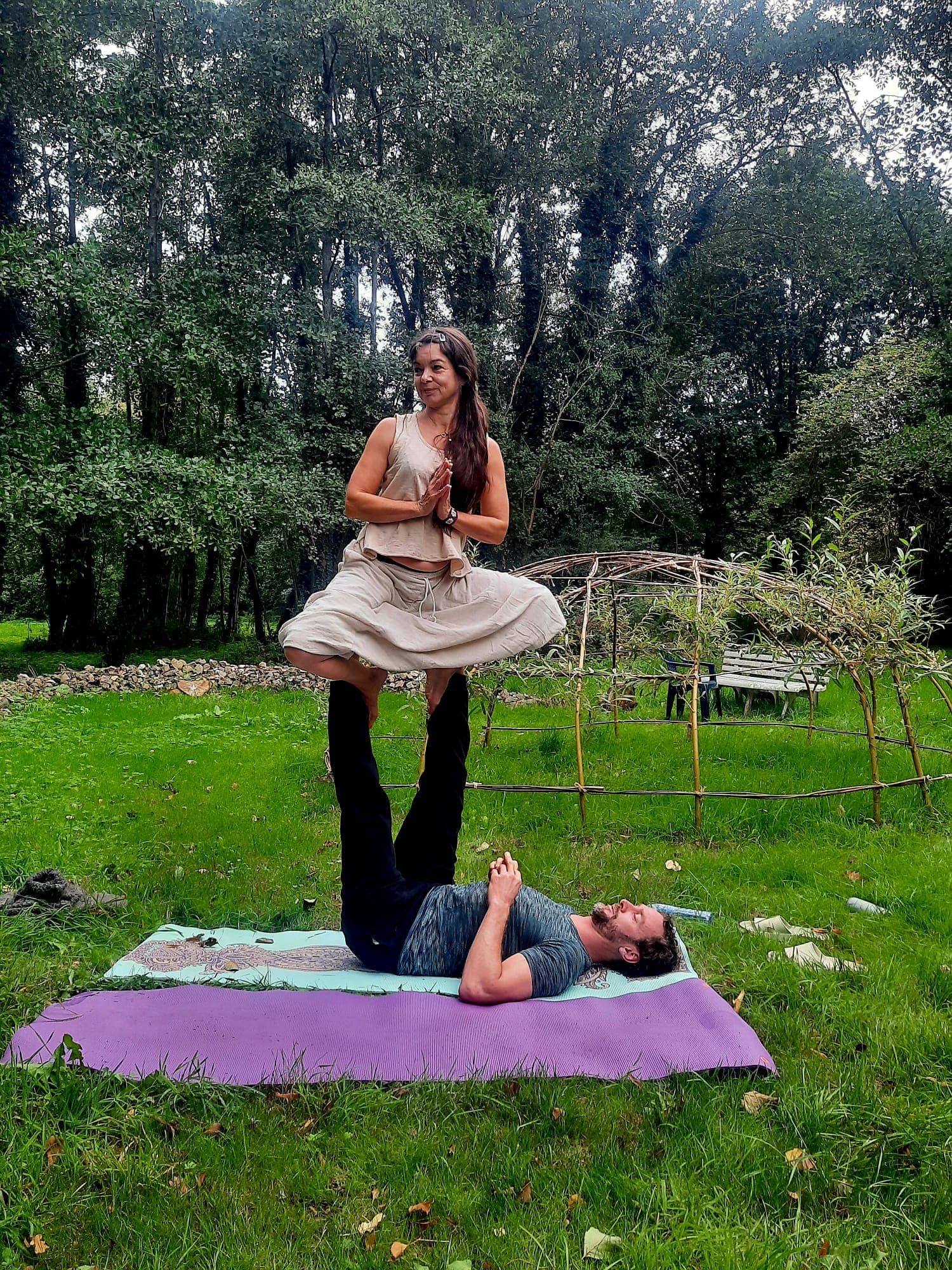 Femme en équilibre sur les pieds d'un homme en posture d'acro-yoga dans un jardin.