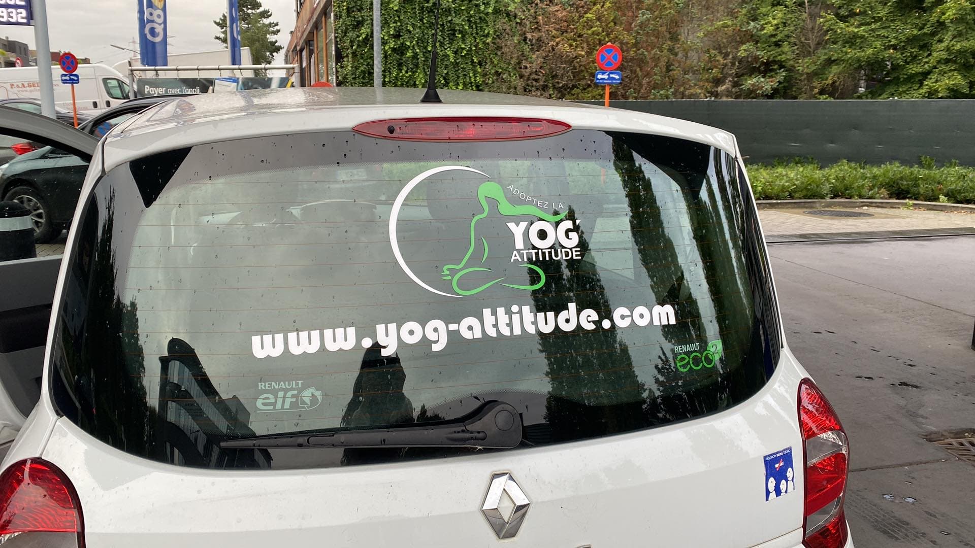 Logo et site web de Yog-Attitude sur la vitre arrière d'une voiture blanche.